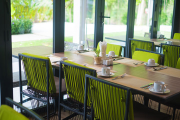 Empty restaurant part of hotel with table and armchair near windows and garden view.