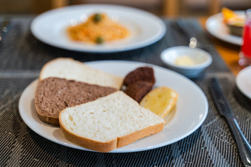 Fresh romantic breakfast table next to morning briliant light window, with bread, pastry, spaghetti, fruit, juice, coffee cup