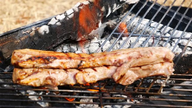 キャンプ場で炭火で炙りながらベーコンの塊を焼く