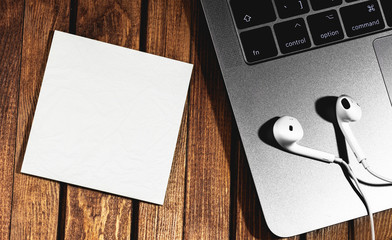 wooden table with laptop and white headphones, clear note