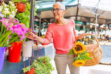 Attractive mature woman shopping in an outdoors fresh flowers market stall, buying and picking from...