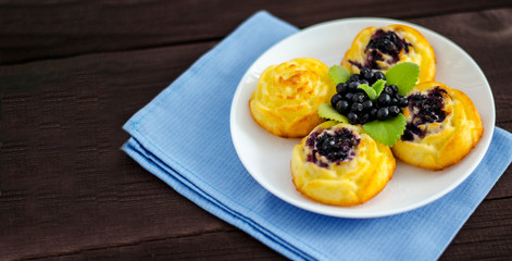 On the dish are three cheesecakes with blueberries and one without toppings, garnished with fresh blueberries and mint leaves. Composition on a textile napkin.