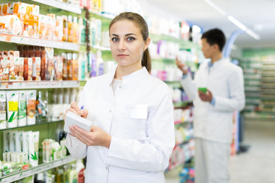 Woman is checking medicine with notebook in shelves in apothecary