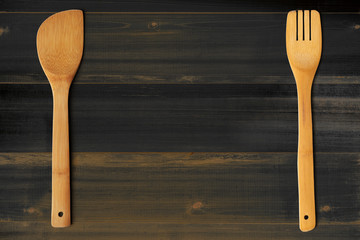 Wooden stirrer and fork on dark wooden table. Kitchen and cooking concept.