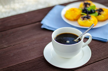 On the dish are three cheesecakes with blueberries and one without toppings, garnished with fresh blueberries and mint leaves. Composition on a textile napkin with a cup of coffee.