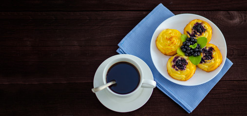 On the dish are three cheesecakes with blueberries and one without toppings, garnished with fresh blueberries and mint leaves. Composition on a textile napkin with a cup of coffee.