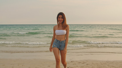 Asian woman walking on sand beach. Young happy female in bikini relax and fun walking near tropical sea when sunset while holiday, vacation, summer trip concept.