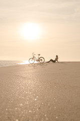 Fototapeta premium Beautiful blonde woman and bicycle traveling down a quiet beach at sunset.