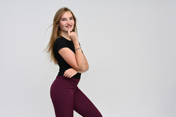A knee-length portrait of a pretty brunette girl with long flowing hair in a black T-shirt and burgundy trousers on a white background. Smiling, showing emotions.
