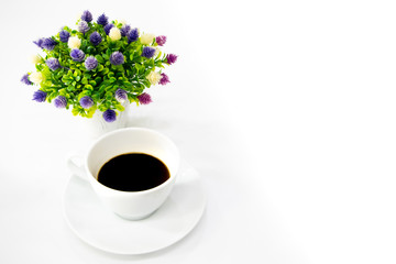 A cup of coffee with a small vase of flower on white desk. A good starting in the early morning to get ready for a day.Free copy space on right for text or design