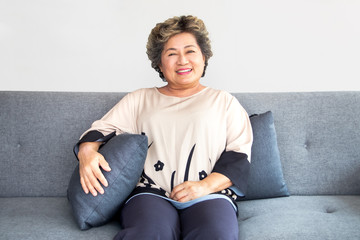 A happy asian senior woman sit on couch at home with smile and have make up on face. Concept of beautiful elderly woman, smiling and anti-aging.