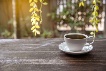 Hot cup of coffee on wooden tabletop on blurred green nature bokeh background