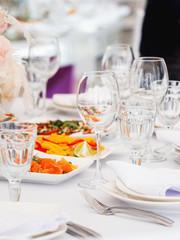 Table served for wedding banquet with cutlery and flowers in vases. Pastel colored decorations.