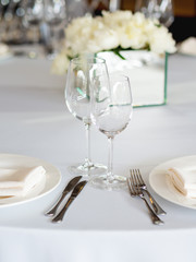 Table served for banquet with cutlery, wine glasses and napkins. Pastel colored decorations.