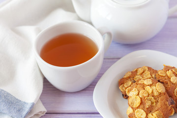 Cup of tea with cookies over lilac wooden background