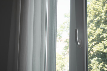 Inside view through an open window with light white curtains