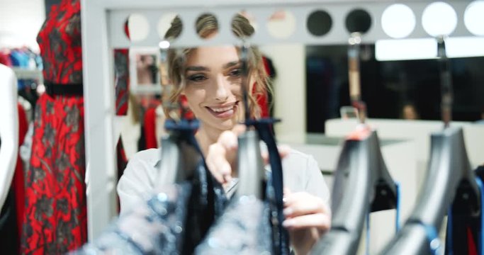 Pretty smiling lady in fashionable clothing and trendy hairdo choosing new outfits in clothing store during sales, consumerism