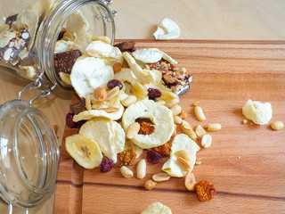 Dehydrated fruit of apple, banana, raisins, rhubarb and nuts from a glass jar on a wooden board.