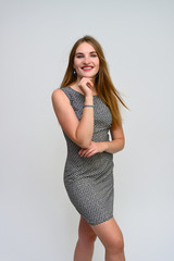 Fototapeta premium Vertical portrait of a pretty secretary manager brunette girl with long fluttering hair in a gray dress on a white background. Smiling, showing emotions.