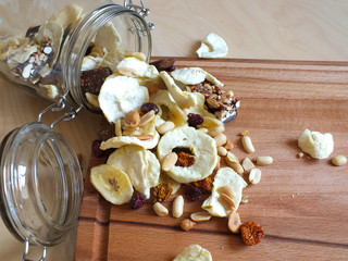 Dehydrated fruit of apple, banana, raisins, rhubarb and nuts from a glass jar on a wooden board.