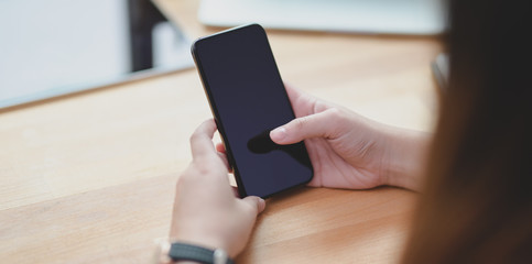 Close-up view of young female holding smartphone on wooden table