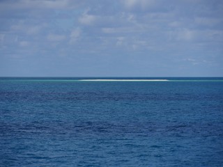 Wide shot of the ocean with a sliver of a white sand bar in the distance