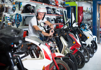Portrait of glad male in helmet on motorbike in the store