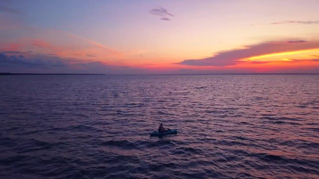A dramatic drone shot of a lone kayaker slowly driffting into a colorful sunset