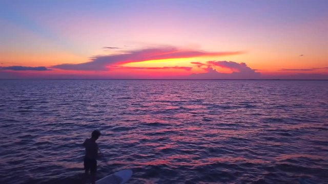 A dramatic drone shot of a kayaker and padlle boarder slowly driffting into a colorful sunset