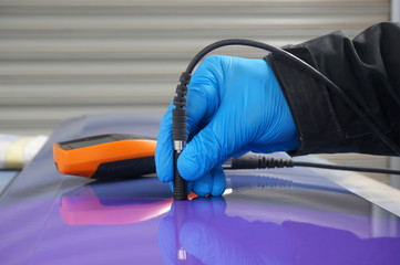 Person using probe, with digital tester, to measure the paint thickness microns on a painted metal...