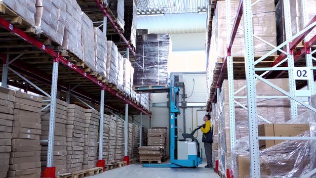 warehouse worker driver in uniform loading cardboard boxes by forklift stacker loader
