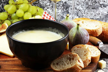 Gourmet Swiss fondue dinner on a winter evening with assorted cheeses on a board alongside a heated pot of cheese fondue with two forks dipping