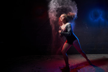 Young teen girl in a dark room during a photoshoot with flour with a colored light and a black background