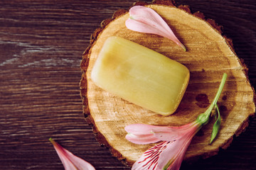 Removing stains with bile( gall, sap) soap bar. Natural chemical free household clothing washing products concept. Soap bar on natural wooden disc with decorative blossom, flat lay view, copy space.
