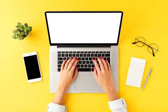 Woman’s hand working on laptop with empty screen. Business background with mobile phone, notebook, pen and eyeglasses. Top view