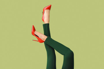 Legs of young woman in high-heeled shoes and pants on color background - obrazy, fototapety, plakaty