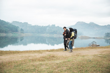 Obraz premium couple hikers with backpacks enjoying lake view, walking side the lake