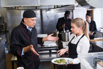Waitress with dish talking with puzzled chef