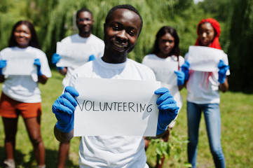 Naklejka premium Group of happy african volunteers hold blank board with volunteering sign in park. Africa volunteering, charity, people and ecology concept.