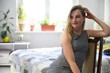 Portrait of a sexy pretty happy brunette girl with long waving hair in the room. Sits, smiles, shows emotions.