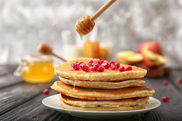 Pouring of honey from spoon onto tasty pancakes on table