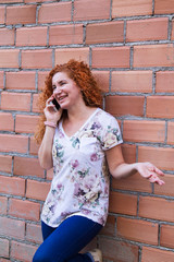 woman talking and gesturing with her cell phone leaning against the wall