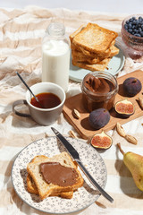 Appetizing toasts with chocolate paste, tea, figs, blueberries and almonds on the table.