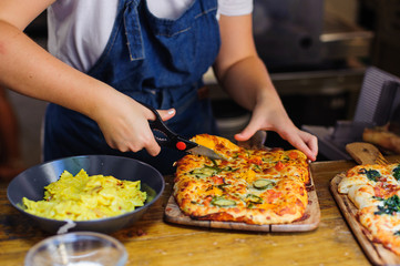 Obraz na płótnie Canvas Chef hands cuts pizza with kitchen scissors