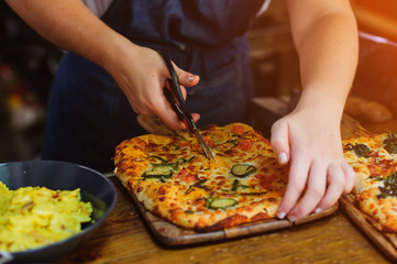 Chef hands cuts pizza with kitchen scissors