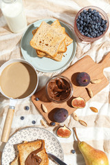 Appetizing toasts with chocolate paste, coffee with milk, figs and blueberries on the table.