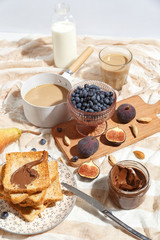 Appetizing toasts with chocolate paste, coffee with milk, figs and blueberries on the table.