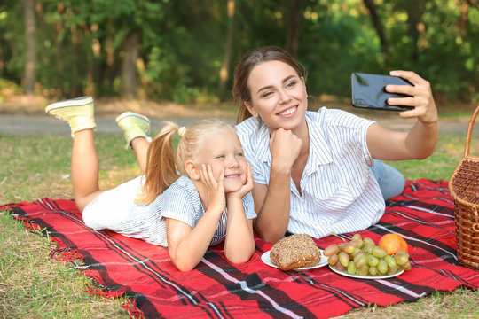 Happy mother and daughter taking selfie during picnic outdoors