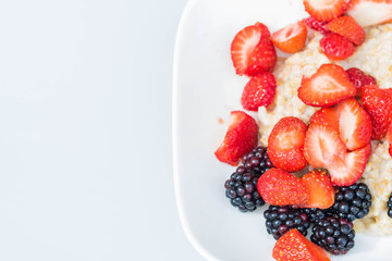 Close-up white bowl dish with oatmeal porridge with strawberries and blackberries. View from above. The concept of healthy vegetarian food and delicious breakfasts. DIY harvest. Copy space