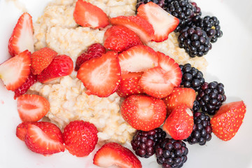 Close-up white bowl dish with oatmeal porridge with strawberries and blackberries. View from above. The concept of healthy vegetarian food and delicious breakfasts. DIY harvest